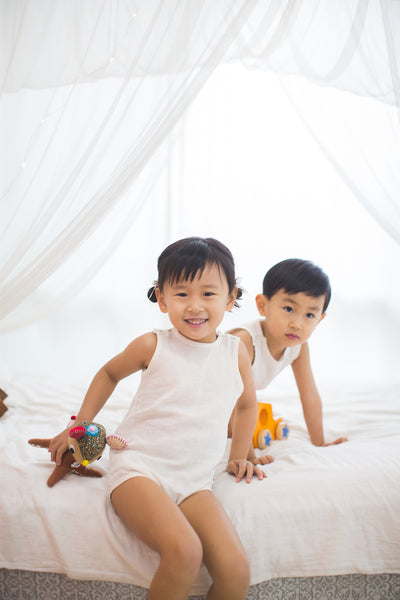 toddler boy and girl smile wearing dye free GOTS certified organic cotton bodysuit sitting on bed