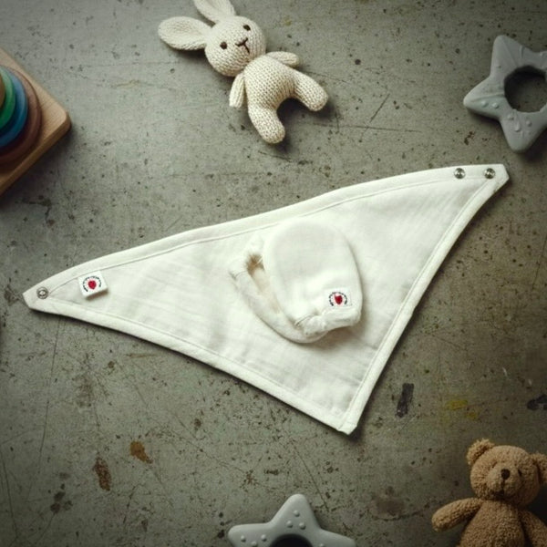 White triangle-shaped baby blanket with embroidered design on a textured surface with toys around