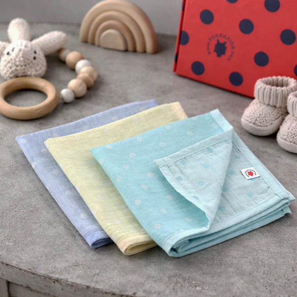 Set of folded eczema safe baby wash clothes in pastel colors on a concrete surface with toys in the background.