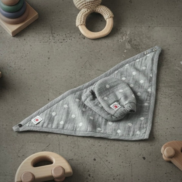 Gray triangle-shaped baby blanket with white polka dots on a concrete surface with toys around