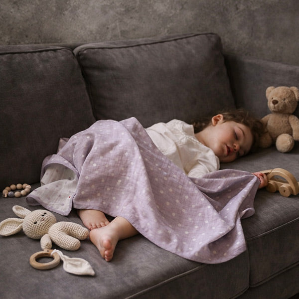 Pokka Kids purple GOTS organic cotton swaddle blanket covering toddler baby sleeping beautifully on luxury couch