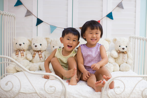 Toddler boy and girl with eczema wearing Pokka Kids 100 % GOTS certified organic cotton baby bodysuits smiling on day bed