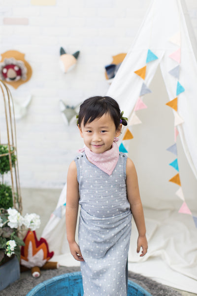 Toddler girl wearing GOTS Certified organic cotton polka dot bandana bib in pink, bodysuit, and blanket as sarong in gray