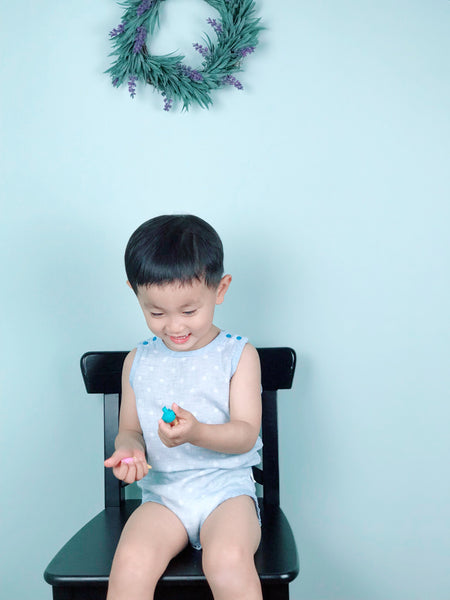 Toddler boy wearing blue GOTS certified organic cotton sleeveless baby bodysuit sitting on a chair